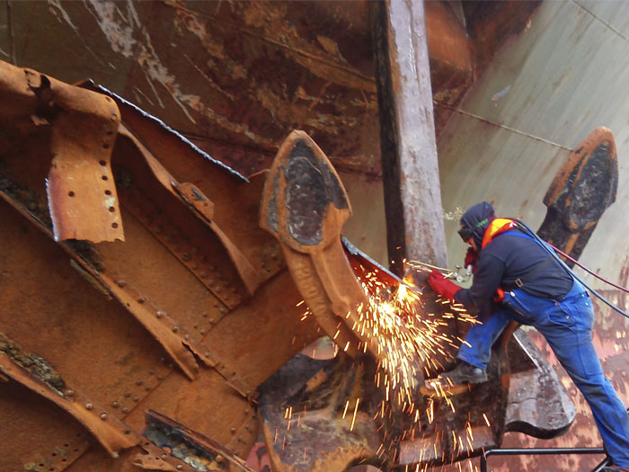 Schiffsbauer zerschneidet mit dem Scheidbrenner ein kaputtes Schiff..