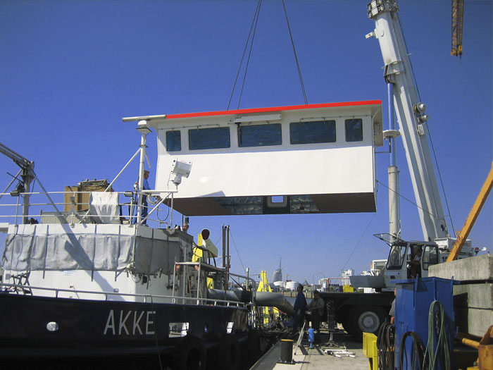 Ein Kran hebt einen Schiffsaufbau an Deck.